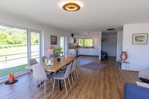 Une cuisine moderne dotée de grandes fenêtres, un coin repas avec une table et des chaises en bois, et une vue sur la verdure environnante.