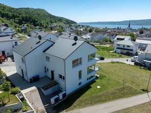 A two-story residential building with a flat roof, a balcony, and a view of a lake and hills.