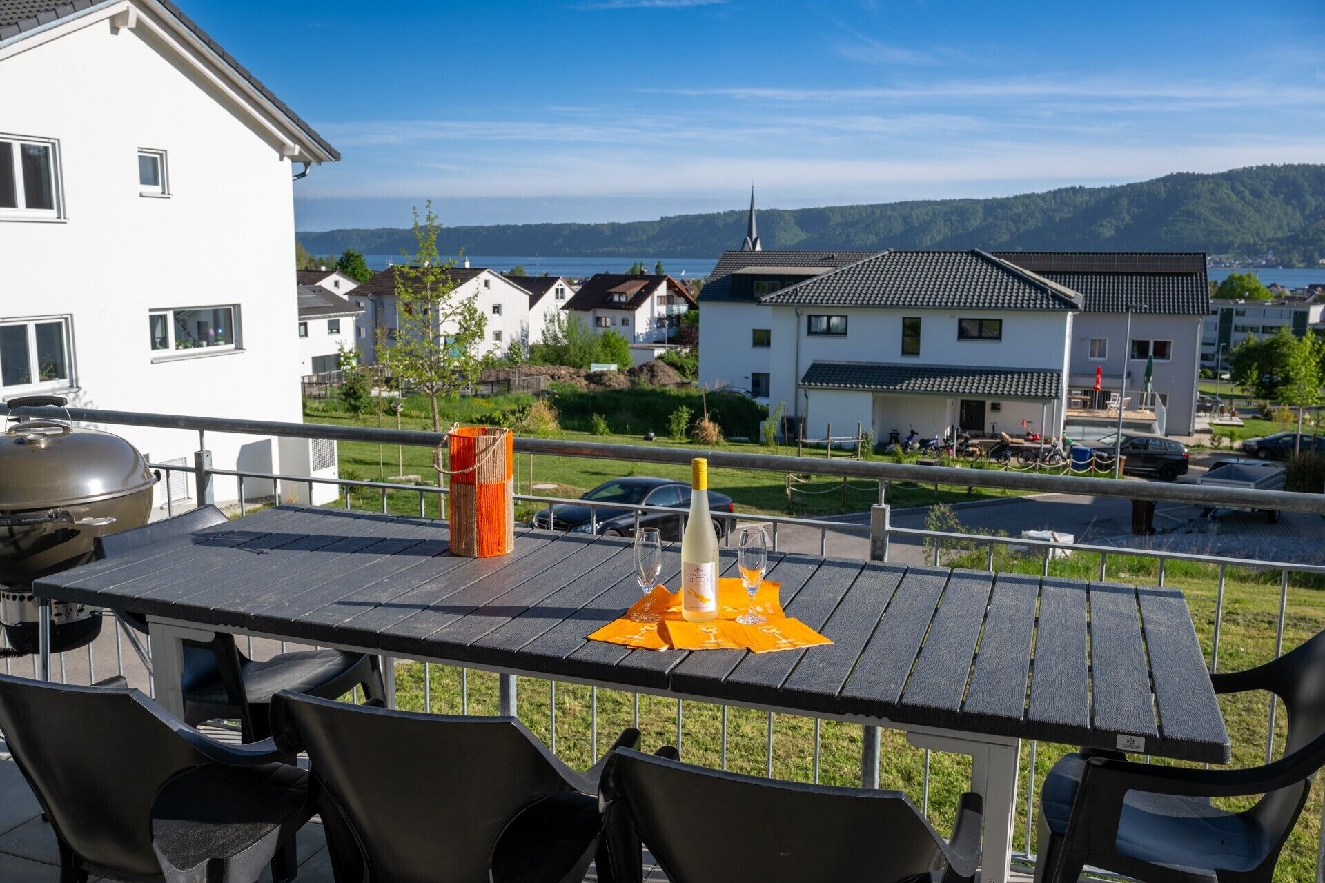 Un balcon avec une table, des chaises, un barbecue et une bouteille de vin.