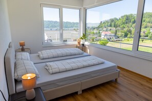 Un dormitorio con un ventanal grande, una cama, una mesita de noche con lámpara y vistas a un paisaje verde.