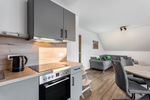 Een moderne keuken met een ingebouwde oven en koffiezetapparaat, een eethoek met een tafel en stoelen, en een grijze bank met kussens.