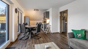 Interior moderno com área de refeições, cozinha e sala de estar com sofá e almofada verde.