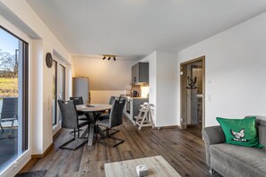 A modern interior with a dining area, kitchen, and a living space with a sofa and a green pillow. - Apartment 'Eierschale' with Mountain View, Balcony and Wi-Fi (Schmallenberg)