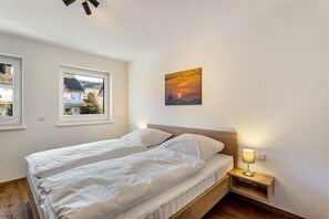 Een slaapkamer met een bed, nachtkastje, lamp en een schilderij van een zonsondergang.