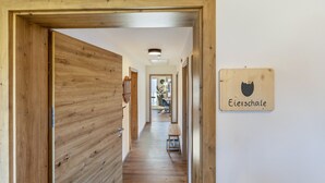 Corredor interno de madeira que dá para um quarto com porta de madeira, um banco e uma placa fixada na parede com silhueta de urso e texto.