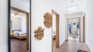 Un intérieur moderne avec un plancher en bois, un lit, une œuvre d’art en bois fixée au mur et un coin repas visible à travers une porte ouverte.