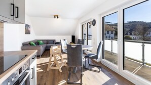 Une cuisine moderne avec un coin repas, un canapé et une vue sur un quartier résidentiel grâce à de grandes fenêtres.