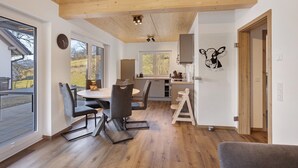 Uma cozinha moderna com vigas de madeira no teto, área de refeições com mesa e cadeiras, e uma grande janela com vista para o exterior.