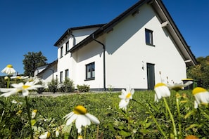 Une maison moderne à deux étages, avec une façade blanche, de nombreuses fenêtres et un toit en pente.