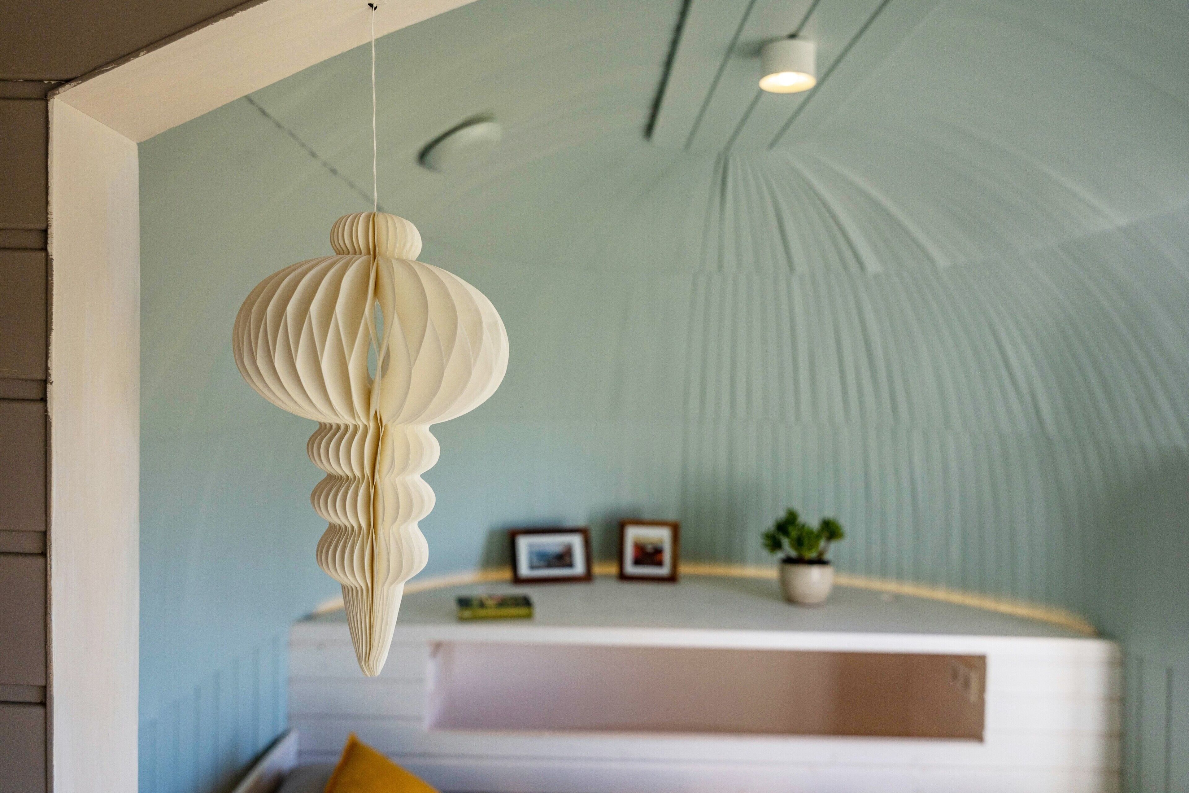 Una habitación con un farolillo de papel colgante, un banco blanco y una pequeña planta en maceta.