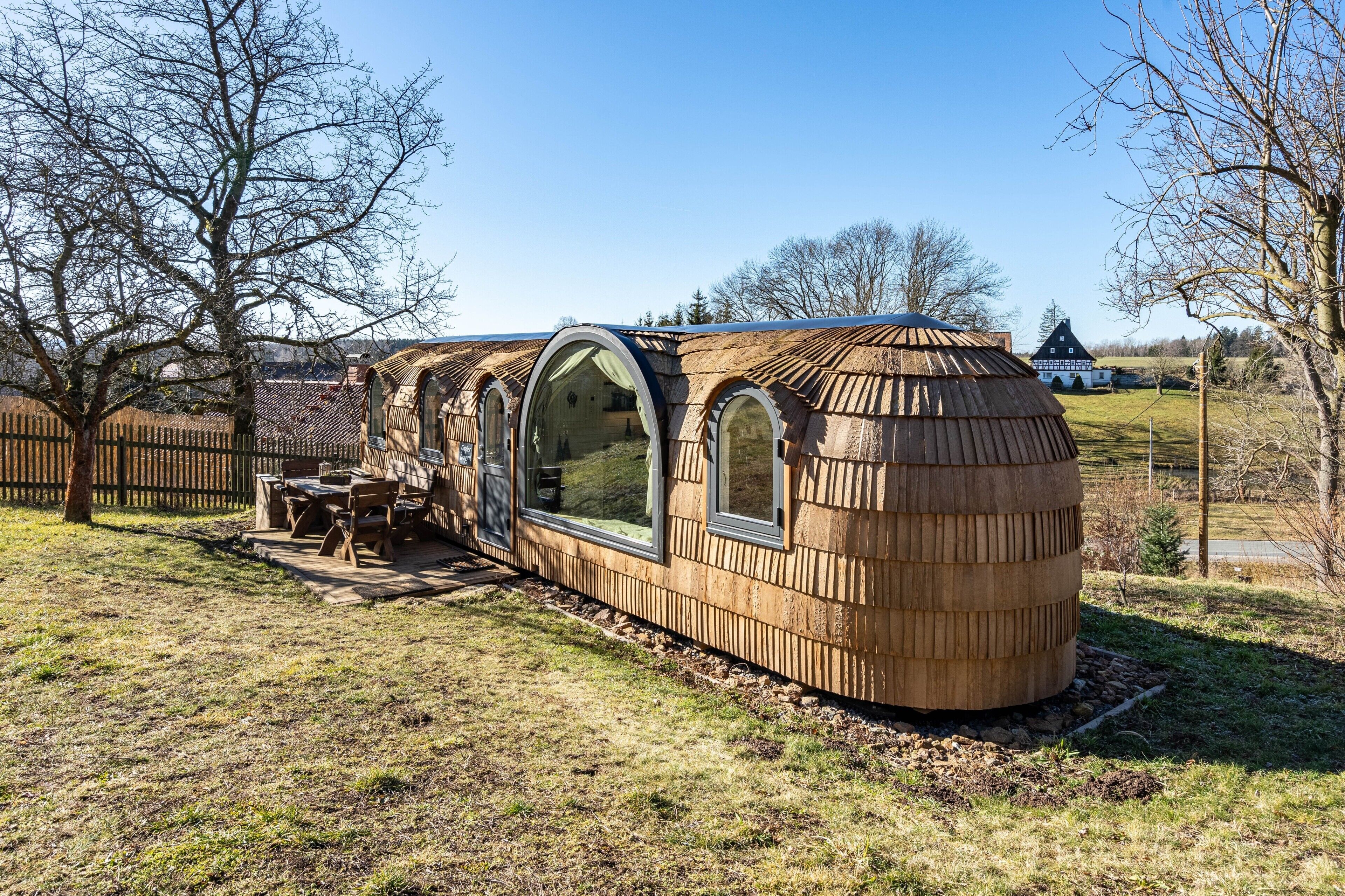 Eine Holzhütte mit großen Fenstern und einer Tür, umgeben von einer Wiese und Bäumen.
