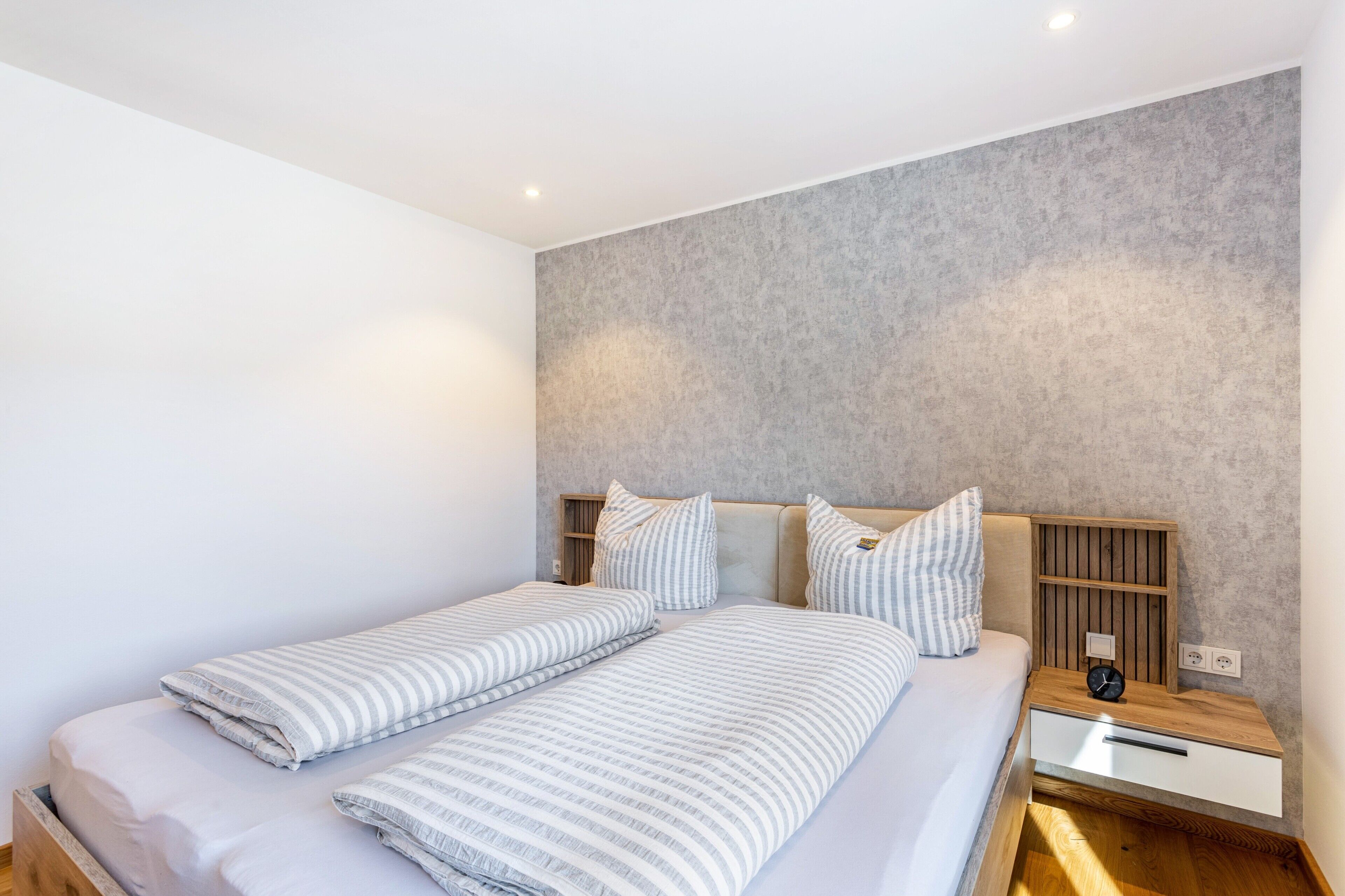 Ein Schlafzimmer mit zwei Betten, einem Holz-Nachttisch, einer Nachttischlampe und einem Wandregal.