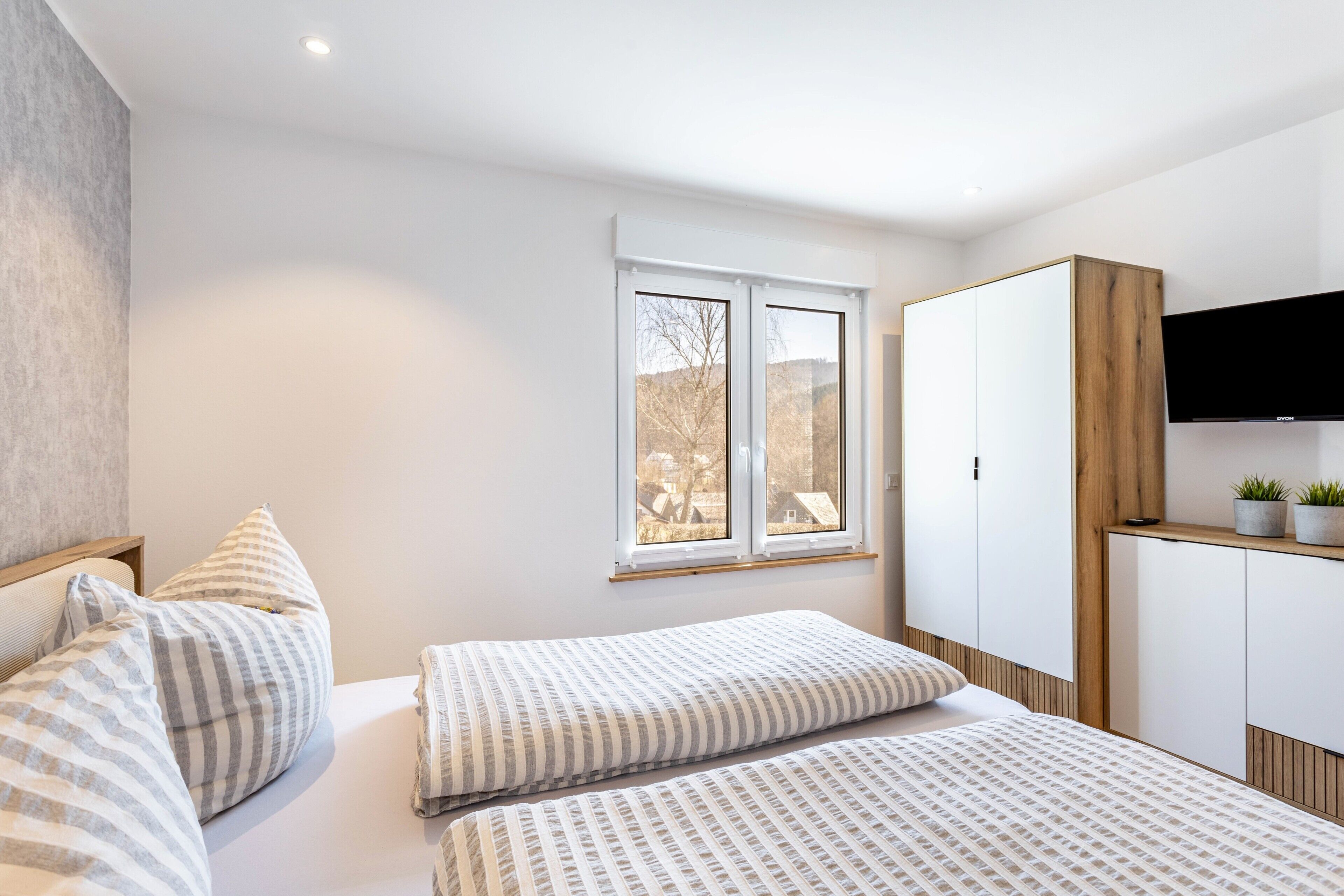 Ein Schlafzimmer mit zwei Betten, einem Fenster, einem Kleiderschrank und einem Fernseher.