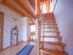 Una escalera de madera que lleva a un nivel superior, suelo de madera, un estante con objetos y una ventana.