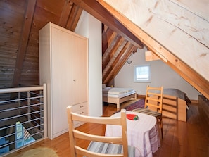 A loft bedroom with a wooden ceiling, a bed, a chair, a wardrobe, and a window.