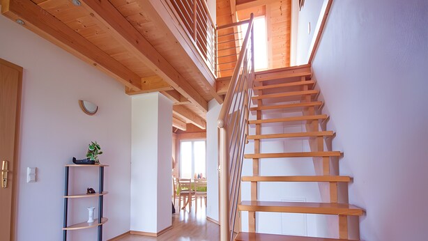 Una escalera de madera que lleva a un nivel superior, suelo de madera, un estante con objetos y una ventana.