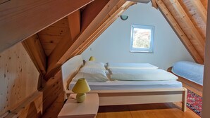 Un dormitorio tipo loft con techo inclinado, una cama individual, una lámpara de noche y un ventanal.