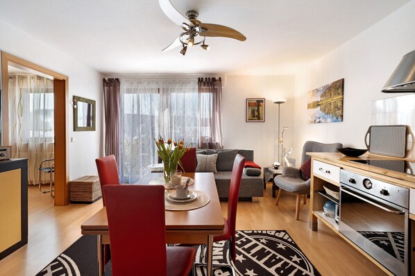 A modern living room with a dining area, a sofa, a TV, and a ceiling fan.