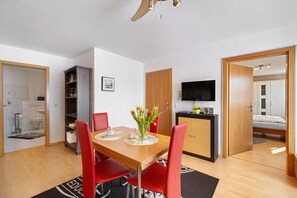 Une chambre moderne avec une table à manger en bois, des chaises rouges, un téléviseur, un lit et un coin cuisine.