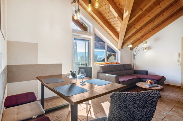 A modern living room with a wooden ceiling, a dining table with chairs, a sofa, and a lamp.