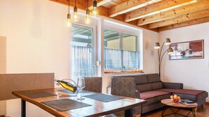 A modern living room with a wooden dining table, two chairs, a sofa, and a coffee table with a book and fruit. - Apartment 'Apfelschnitz' with Shared Garden, Balcony and Wi-Fi (Stockach)