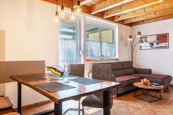 A modern living room with a wooden dining table, two chairs, a sofa, and a coffee table with a book and fruit. - Apartment 'Apfelschnitz' with Shared Garden, Balcony and Wi-Fi (Stockach)