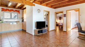 A spacious living area with a kitchen, wooden ceiling beams, a flat-screen TV, and a washing machine. - Apartment 'Apfelschnitz' with Shared Garden, Balcony and Wi-Fi (Stockach)