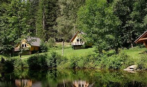 A lakeside cabin with a deck, surrounded by dense forest and a calm lake.