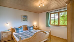A bedroom with a wooden bed, two bedside tables, a nightstand, a window with a view, and a wall-mounted light fixture. - Apartment 'Birke' with Private Terrace, Shared Garden and Wi-Fi (Titisee-Neustadt)