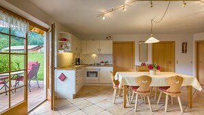 Una cocina con armarios blancos, una mesa de comedor con sillas, una cafetera y vistas a través de un ventanal.