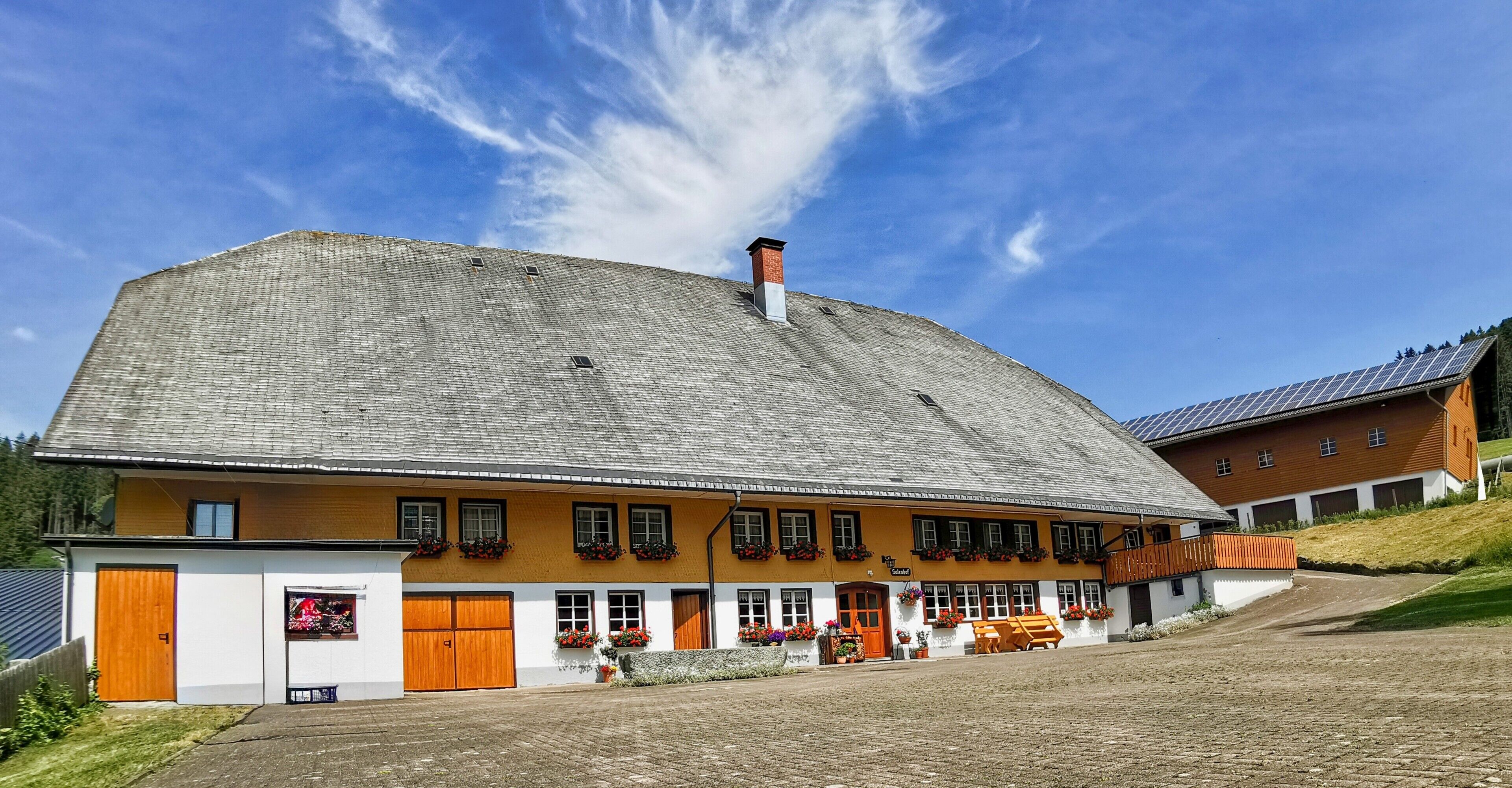 Un grand bâtiment doté de nombreuses fenêtres et portes, d’un toit en pente et d’une cheminée en briques.