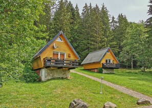Two cabins with balconies, surrounded by lush greenery and a clear sky.