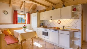 A cozy kitchen with white cabinets, a wooden ceiling, a dining table with a vase of flowers, and a window with curtains. - Apartment 'Fichte' with Shared Garden, Balcony and Wi-Fi (Titisee-Neustadt)