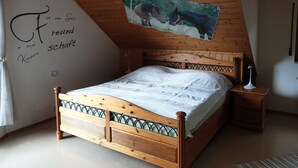 Un dormitorio con techo de madera, una cama con cabecera, una mesita de noche, una pared con un cuadro y una pared con texto.