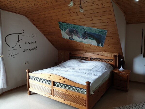 A bedroom with a wooden ceiling, a bed with a headboard, a nightstand, a wall with a picture, and a wall with text.