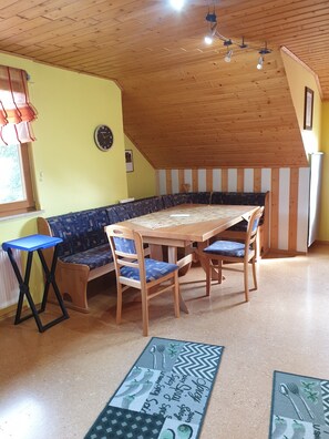 A dining area with a wooden table, blue upholstered bench, and a clock on the wall.