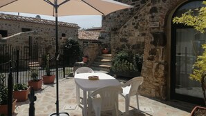 A stone building with a tiled roof, a white table with chairs, and an umbrella providing shade. - Renovated Tuscan-style country house (Castel del Piano)