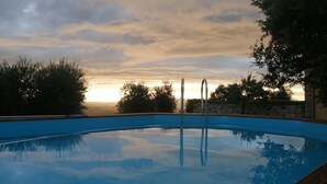 A swimming pool with metal ladders, surrounded by trees and a stone wall, reflecting the sky. - Renovated Tuscan-style country house (Castel del Piano)