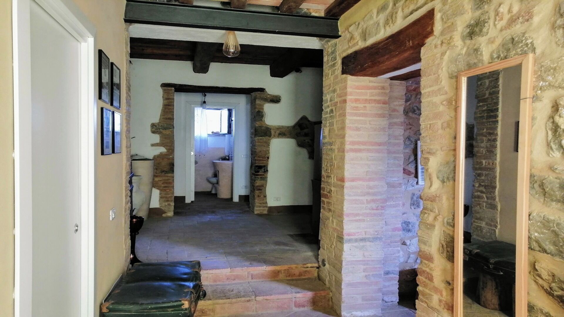 Un étroit couloir en pierre, avec un escalier menant à une pièce dotée d’une porte blanche et d’une fenêtre.