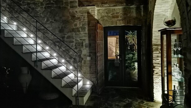 A stone staircase with illuminated steps leading to a door with a glass panel. - Renovated Tuscan-style country house (Castel del Piano)