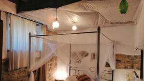 A four-poster bed with a canopy, a bedside table with a lamp, and a stone wall. - Renovated Tuscan-style country house (Castel del Piano)