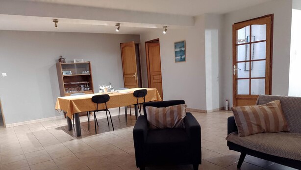 A living room with a sofa, a dining table with chairs, and a kitchen area in the background. - Apartment with garden 30min from Lille! (Vieux-Berquin)
