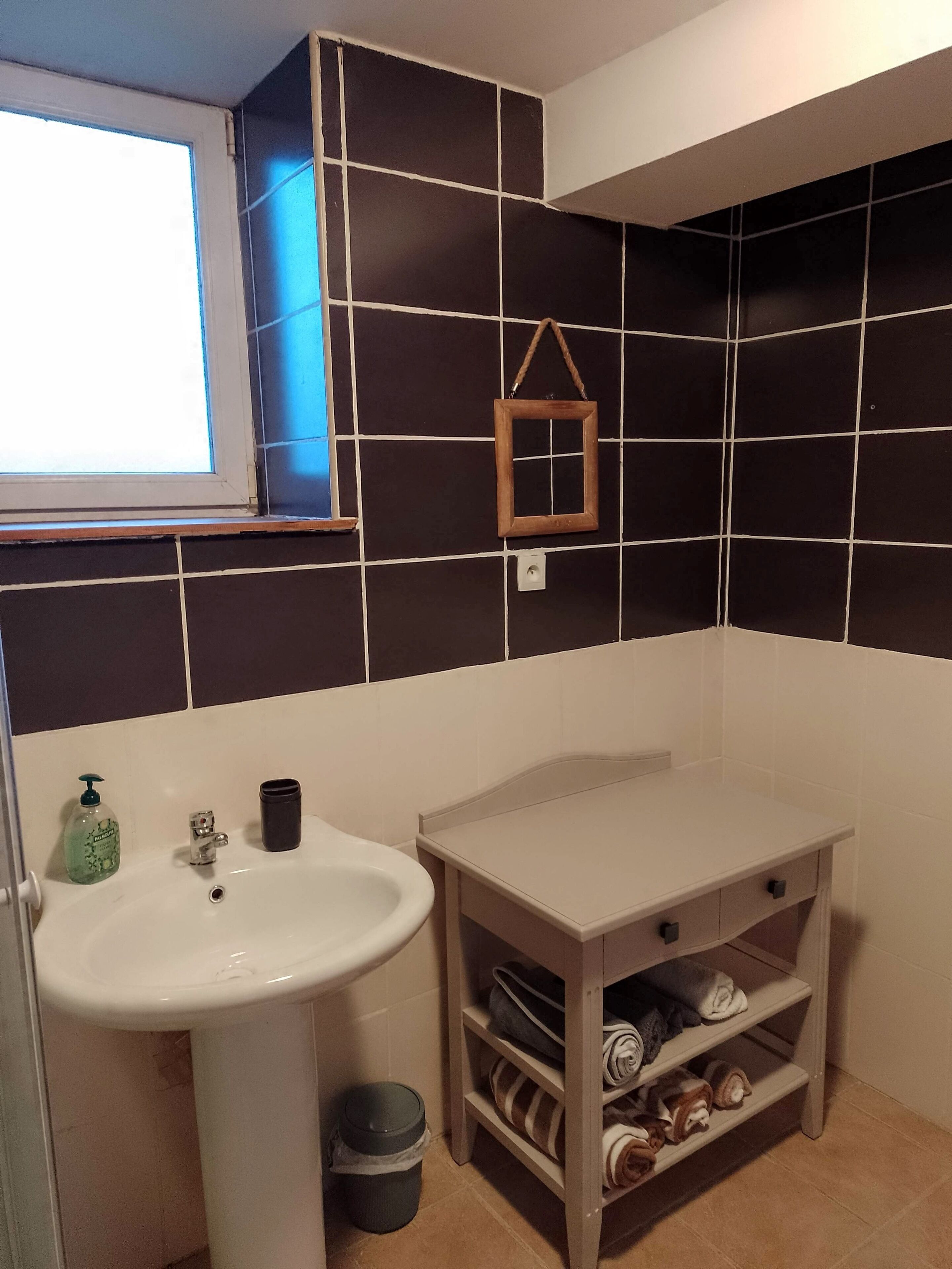Un bagno con un lavandino bianco, uno specchio e uno scaffale con asciugamani.