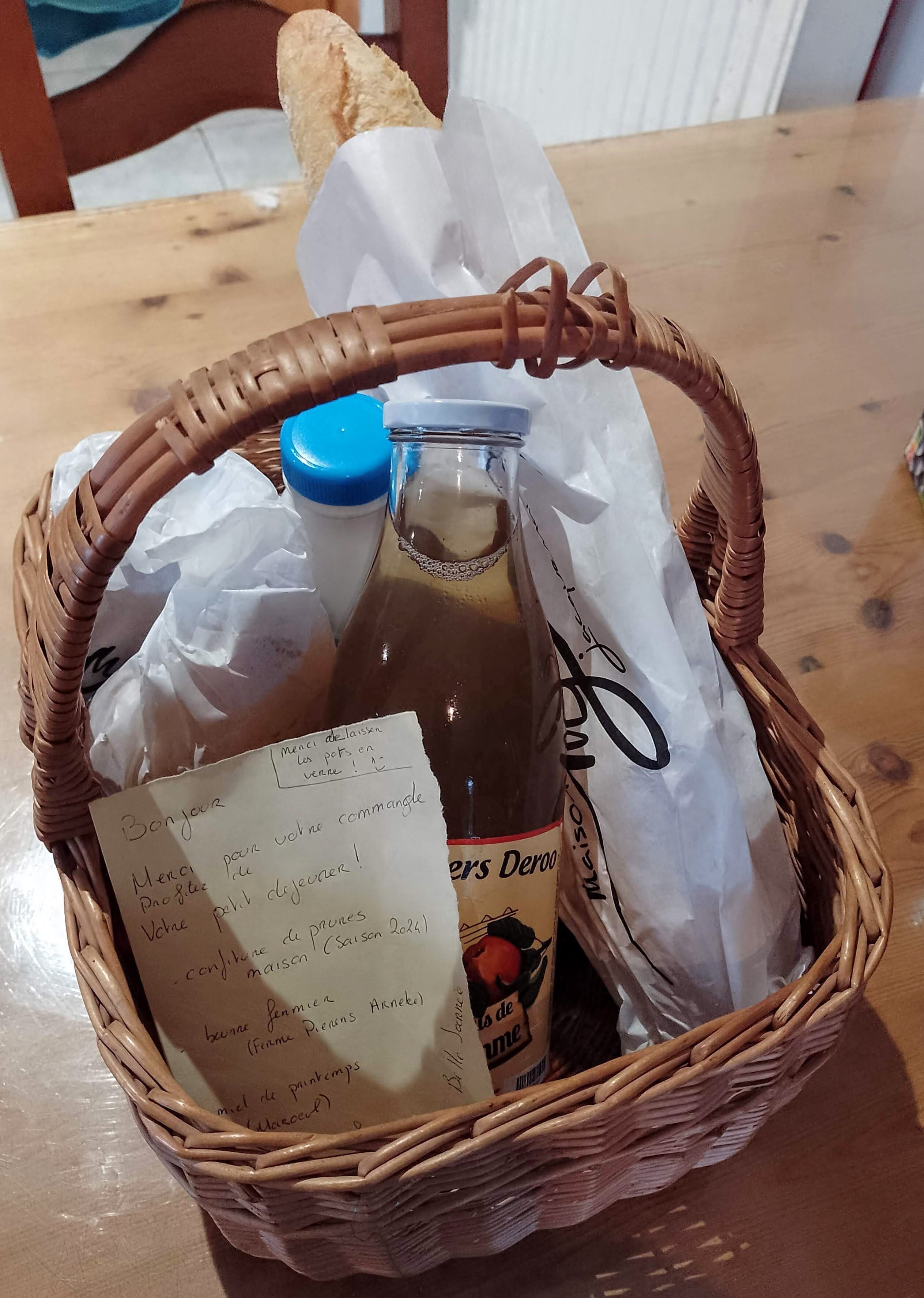 A wicker basket containing a bottle, a plastic bag, and a handwritten note.