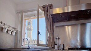 A kitchen with a view of a historic tower through a window, a stainless steel range hood, and a coffee machine.