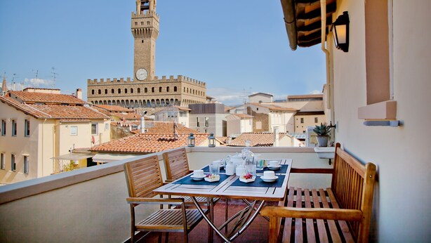 A balcony with a table set for dining, overlooking a historic building with a clock tower.