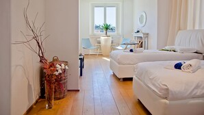 A hotel room with two beds, a small table with a chair, a potted plant, and a view of the outside through a window.