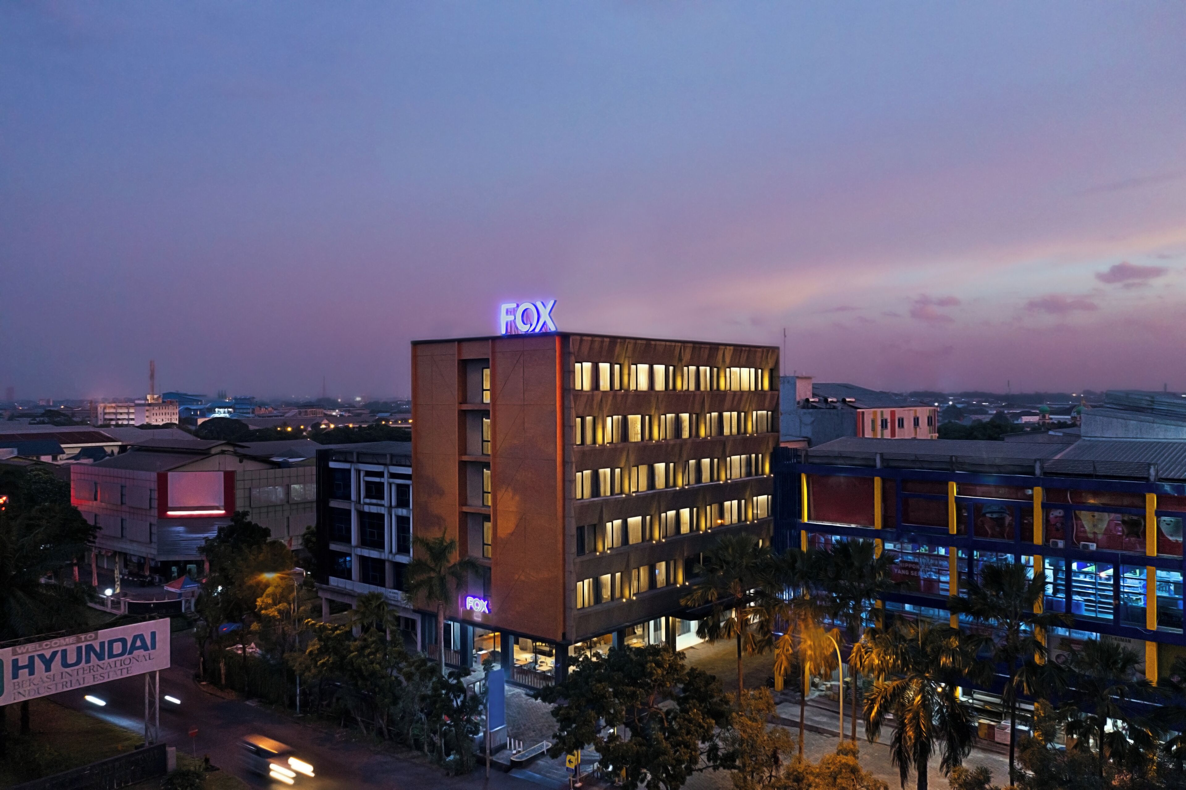 Un edificio moderno con el letrero 'FOX' en la parte superior, rodeado de palmeras y otros edificios.