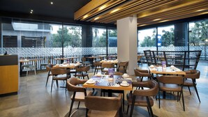 A modern restaurant with wooden ceiling panels, large windows, and a variety of seating arrangements including tables and chairs. - Fox Lite Hotel Cikarang (Cikarang)