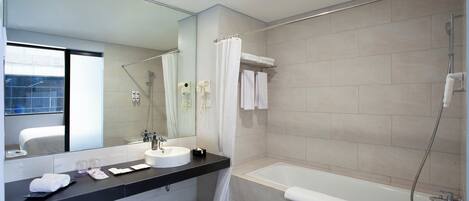 A modern bathroom with a bathtub, a large mirror, a sink, and a toilet.